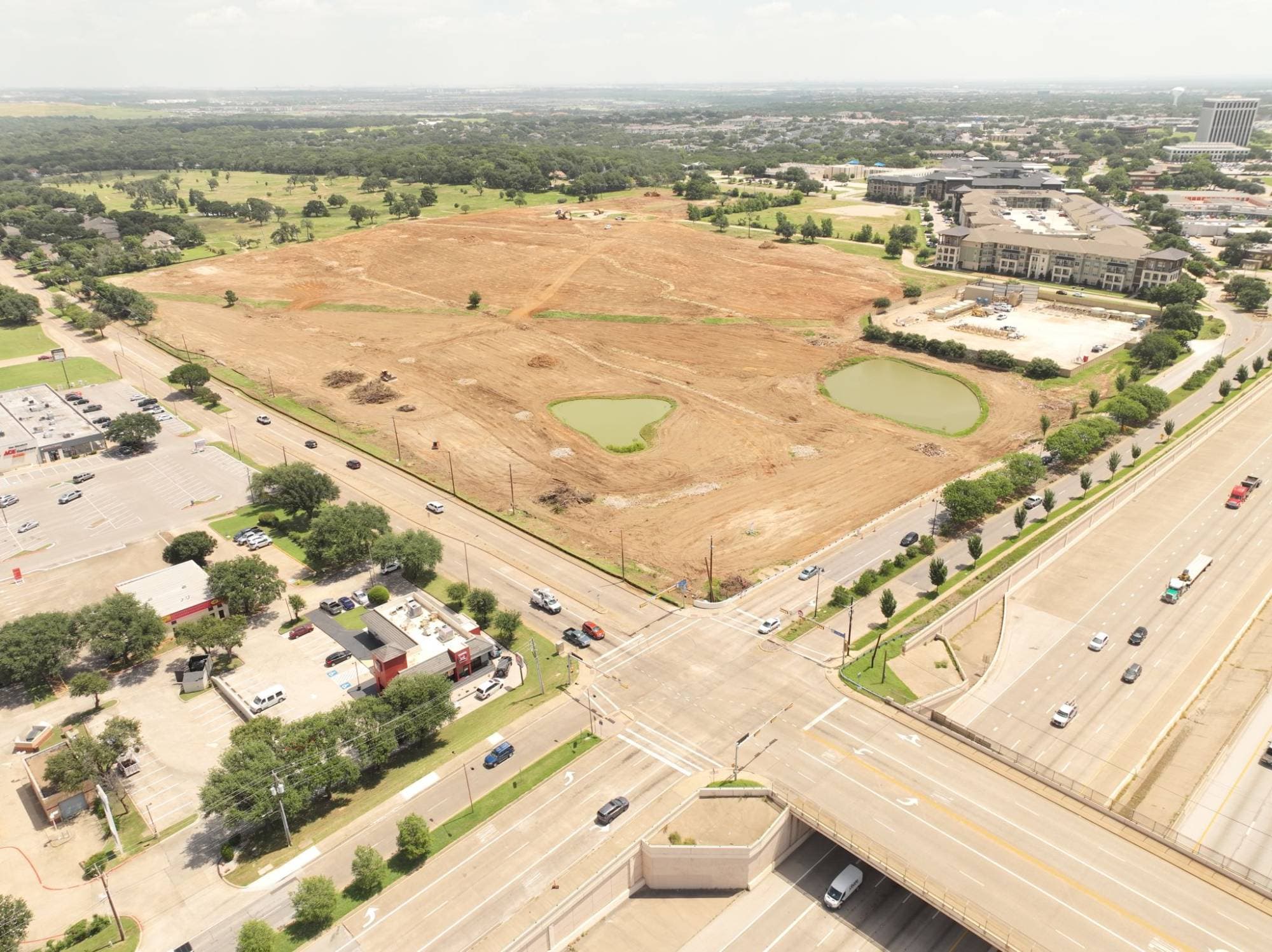 Aerial view of the Rolling Hills site at Cooper & Lamar — cleared and graded for the next phase of construction, with existing retail and residential surrounding the development footprint